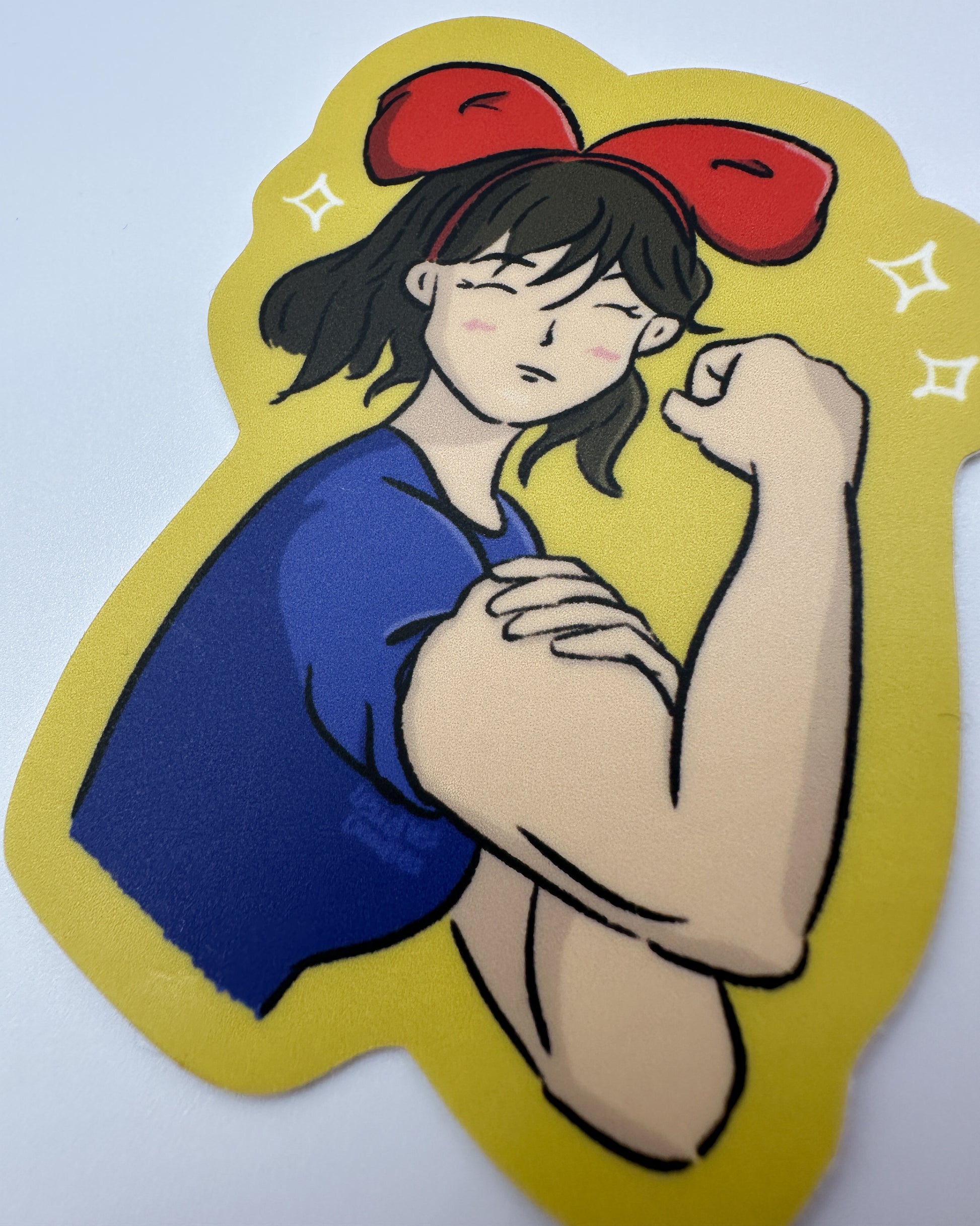 close up photo of matte sticker featuring a woman flexing her arm, and wearing a red bow headband and a blue shirt